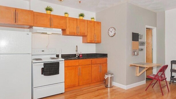 Une cuisine avec des meubles de rangement en bois, une cuisinière blanche, un évier et une petite table à manger avec une chaise.
