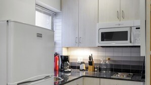 Une cuisine compacte avec des meubles blancs, un four à micro-ondes encastré, un réfrigérateur et une machine à café.