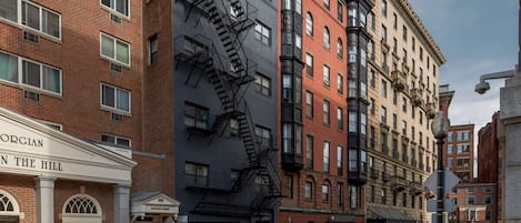 A multi-story building with a fire escape, a sign reading "ORGIAN IN THE HILL," and parked cars on the street.