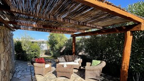 A covered outdoor seating area with stone flooring and wicker furniture. - Holiday Home just 1 km far from Porto Ainu Beach  (Sardegna)