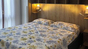 A bedroom with a bed, white curtains, a wooden headboard, and wall-mounted lights. - Holiday Home just 1 km far from Porto Ainu Beach  (Sardegna)