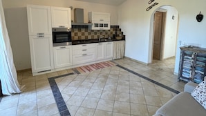 A spacious living area with a sofa, a kitchen with white cabinets, and a tiled floor. - Holiday Home just 1 km far from Porto Ainu Beach  (Sardegna)