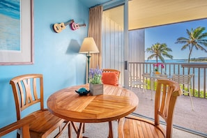Relax in this inviting room with a round table, framed artwork, and a potted plant, leading to an outdoor space with ocean views.