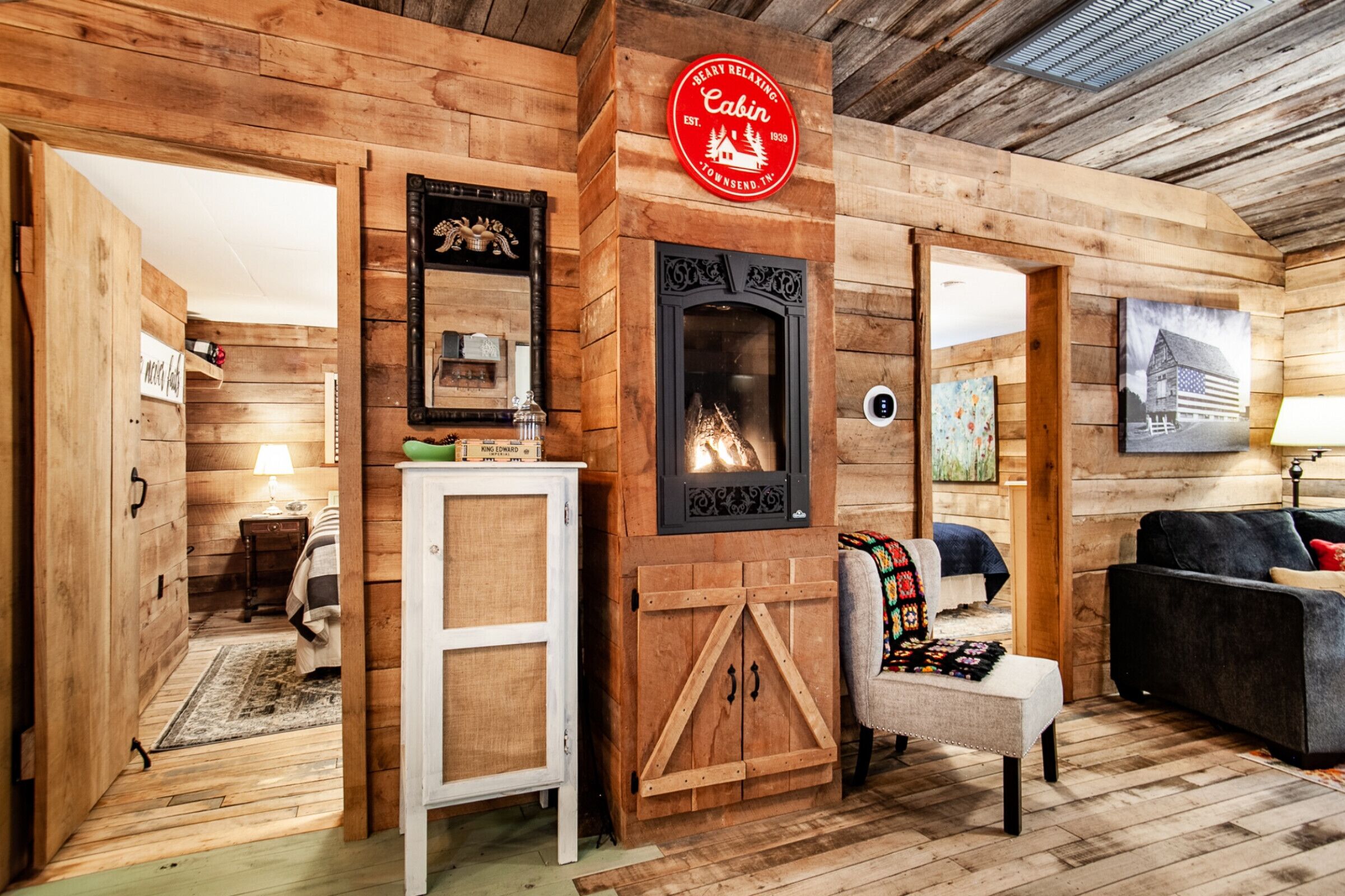Interior acogedor de una cabaña con paredes de madera, una chimenea, un sofá y un televisor montado en la pared.