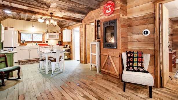L’intérieur d’une cabane est aménagé avec du bois, il comprend un coin repas, une cuisine et une cheminée.