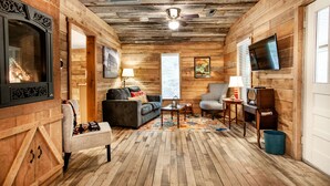 L’intérieur d’un chalet confortable, avec une cheminée, un canapé, un fauteuil à motifs et un téléviseur fixé au mur.