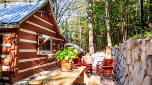 Un chalet rustique avec une table et des chaises en bois, entouré d’un mur de pierres et doté d’une terrasse en bois.