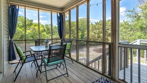 En overdækket udendørs terrasse med et bord og stole, store vinduer og udsigt til træer.