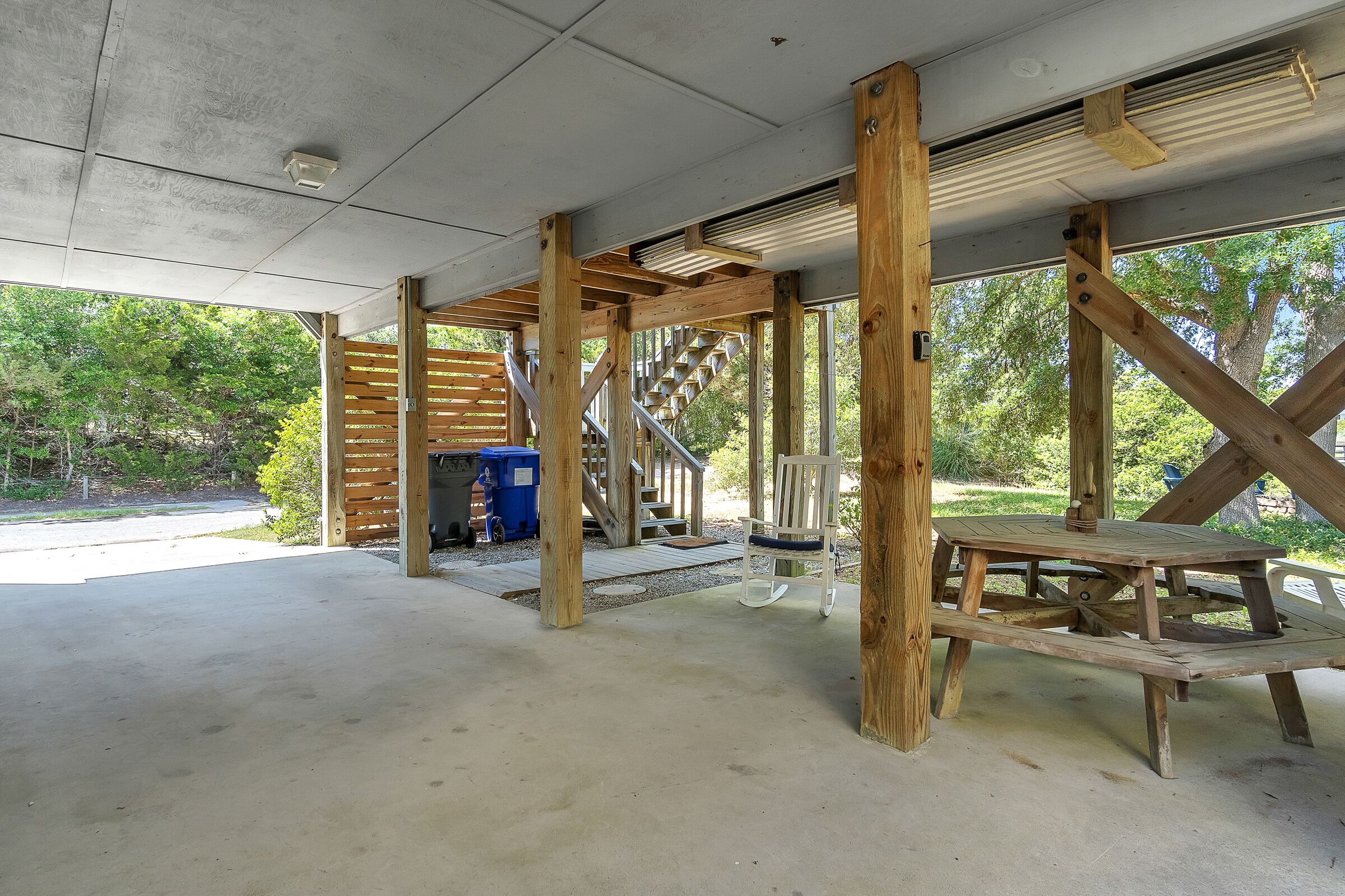 Ein überdachter Außenbereich mit Betonboden, Holzbalken und einer Treppe zu einer höheren Ebene.