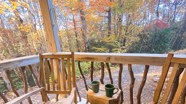 A wooden deck with two wooden chairs and a small table, surrounded by trees with autumn foliage. - Easy Access Cabin deep in the trails but very close to the city! (Murphy)