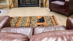 A living room with a fireplace, leather sofa, and a flat-screen TV mounted above the fireplace. - Easy Access Cabin deep in the trails but very close to the city! (Murphy)