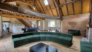 A spacious living area with a curved green sofa, a pool table, and a foosball table. A staircase leads to an upper level, and a brick wall is visible in the background. - So Villa Moulin du Vinet (28) - Heated pool - Basketball - 1h30 Paris - 26p. (Beaumont-les-Autels)