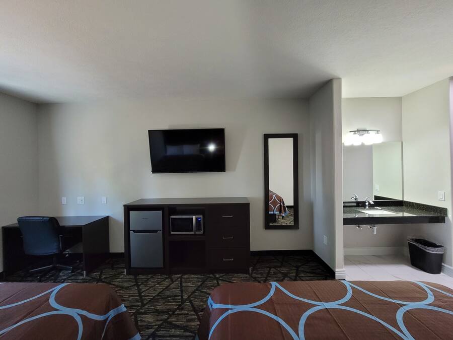 A hotel room with a bed, a desk, a refrigerator, a microwave, a television, and a bathroom with a sink and mirror.