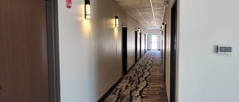 Un largo y estrecho pasillo de hotel con puertas a ambos lados, alfombra estampada y apliques en las paredes.