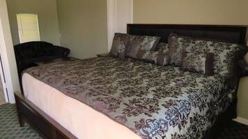 Un dormitorio con una cama grande, cabecera oscura y colcha estampada.