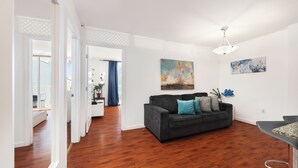 Ein Wohnzimmer mit einem dunklen Sofa, Holzboden und einer Deckenleuchte.