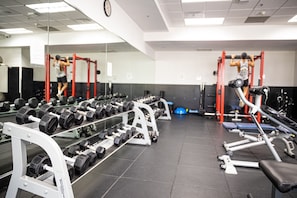 A gym with weightlifting equipment, mirrors, and dumbbells.