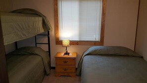 A dormitory room with bunk beds, a bedside table with a lamp, and a window with blinds.