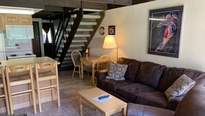 Un salon chaleureux avec un canapé en cuir marron, des chaises en bois, une petite table en bois et un coin cuisine équipé d’un four à micro-ondes et d’une cuisinière.