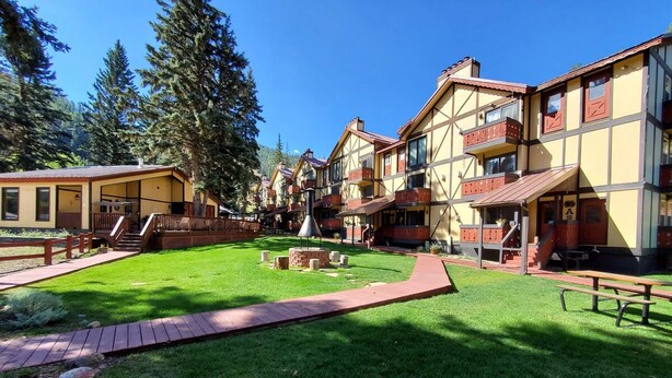 A courtyard with a central fire pit, surrounded by multi-story buildings with balconies and a wooden deck. - Condo in the mountains! (Red River)
