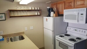 A kitchen with a refrigerator, microwave, stove, and a shelf with glasses and cups. - Condo in the mountains! (Red River)