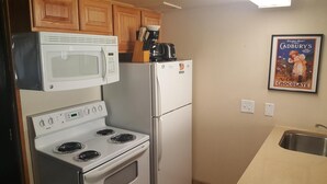 Cozinha compacta com micro-ondas, fogão e geladeira. Há uma cafeteira e um quadro na parede.