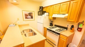 A compact kitchen with wooden cabinets, a stainless steel sink, a gas stove, and a microwave. - Condo in the mountains! (Red River)