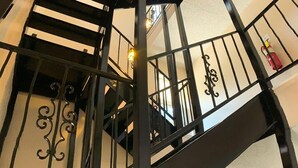 Una escalera en espiral negra con barandales y pasamanos ornamentados, que conduce a un piso superior.