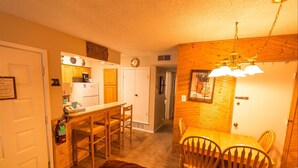 A cozy kitchen with wooden cabinets, a dining area with a table and chairs, and a private room indicated by a sign. - Condo in the mountains! (Red River)