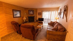 A cozy living room with a fireplace, a television, and a sofa. - Condo in the mountains! (Red River)