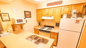 A compact kitchen with wooden cabinets, a microwave, a stove, and a refrigerator. - Condo in the mountains! (Red River)