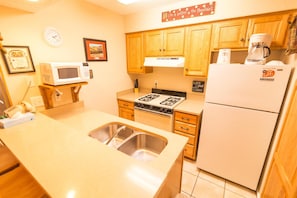 A compact kitchen with wooden cabinets, a microwave, a stove, and a refrigerator.
