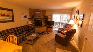 A cozy living room with a fireplace, a television, and a dining area with a table and chairs. - Condo in the mountains! (Red River)