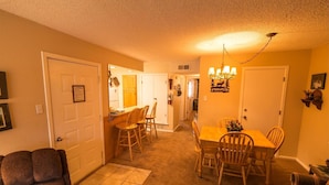 A cozy living room with a fireplace, a dining area with wooden furniture, and a hallway leading to other rooms. - Condo in the mountains! (Red River)