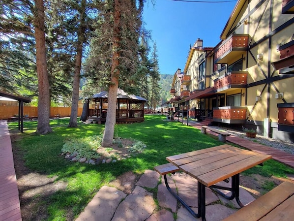 A courtyard with a wooden picnic table, a gazebo, and multi-story buildings with balconies.