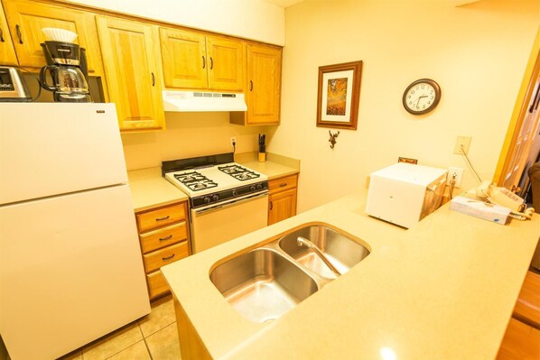A compact kitchen with wooden cabinets, a stove, a sink, and a coffee maker. - Condo in the mountains! (Red River)