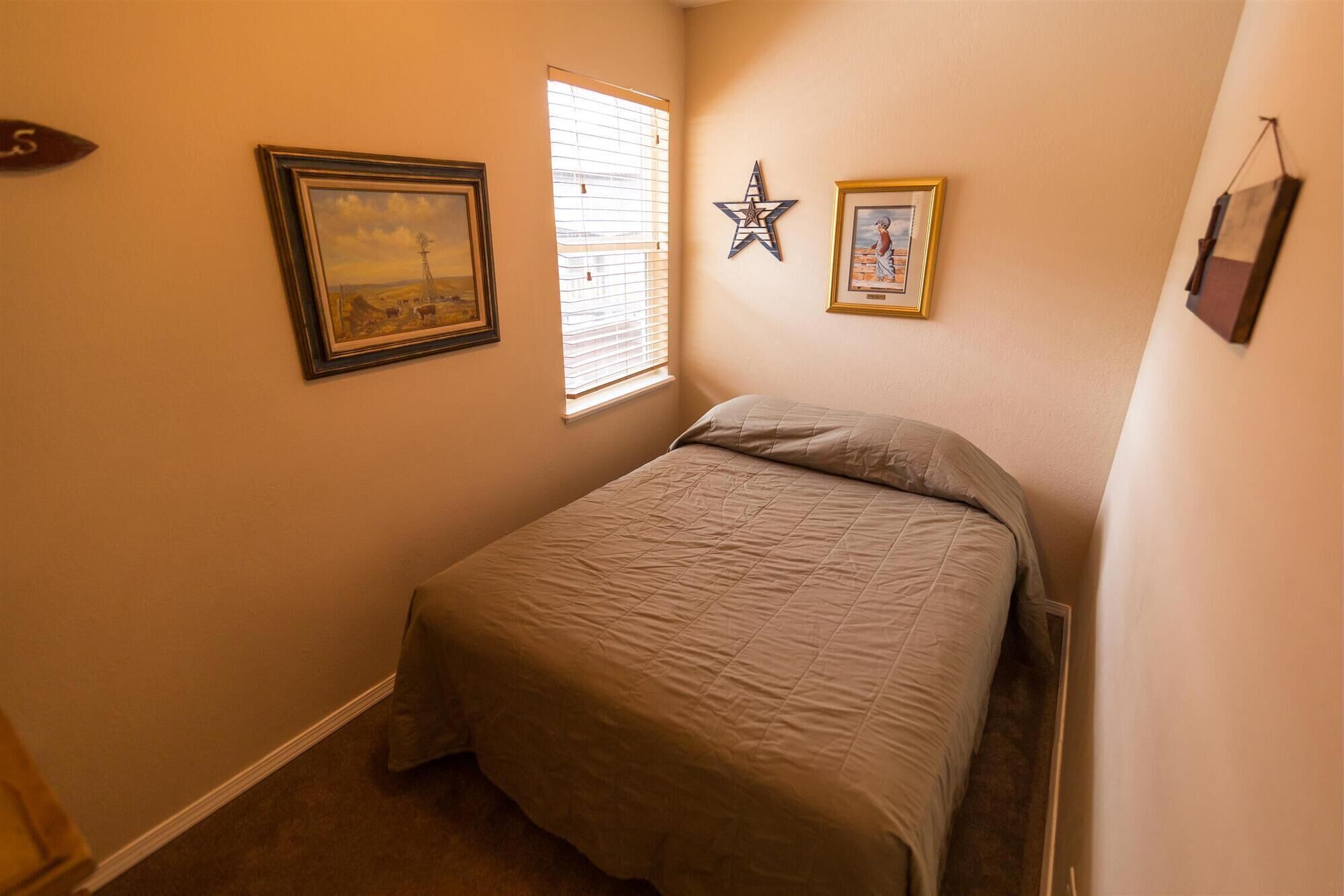 A bedroom with a bed, a window with blinds, and two framed pictures on the wall.