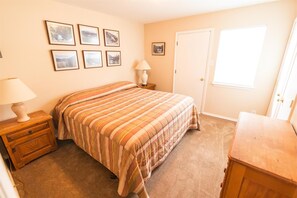 A bedroom with a bed, a nightstand, a dresser, a door, and a window.
