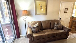 A living room with a brown leather sofa, a framed picture on the wall, and a sliding glass door. - Condo in the mountains! (Red River)