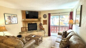 A living room with two leather sofas, a coffee table, a flat-screen TV, a fireplace, and a large window with a view of the outside. - Condo in the mountains! (Red River)