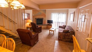 A living room with a sofa, armchair, TV, fireplace, and a staircase. - Condo in the mountains! (Red River)