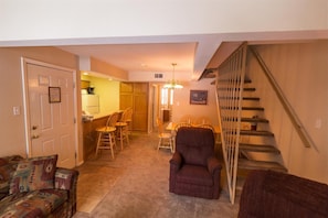 A living room with a sofa, a chair, a staircase, and a kitchen area in the background.