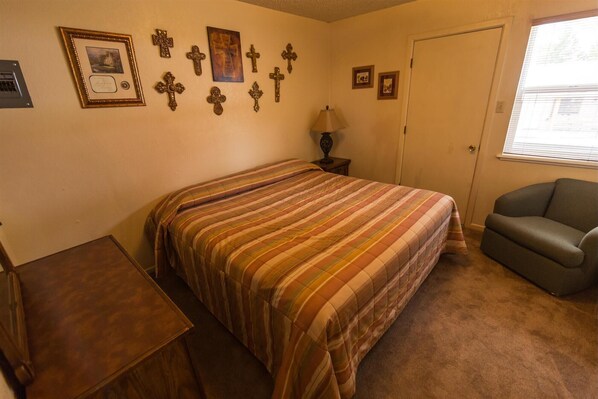 Une chambre à coucher avec un grand lit, une chaise, une table de chevet et plusieurs croix accrochées au mur.