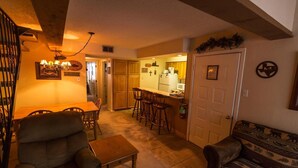 Un salon chaleureux avec un canapé, une petite table et un coin cuisine doté de meubles en bois et d’un tabouret de bar.