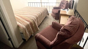 Une chambre à coucher comprenant un lit, une chaise, un bureau, une lampe et un ventilateur de plafond.