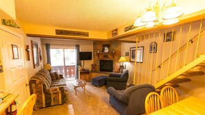 A cozy living room with a sofa set, a television, a fireplace, and a staircase. - Condo in the mountains! (Red River)
