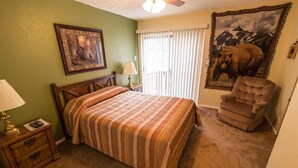 A bedroom with a bed, a chair, a nightstand, a lamp, a painting, and a window with blinds. - Condo in the mountains! (Red River)