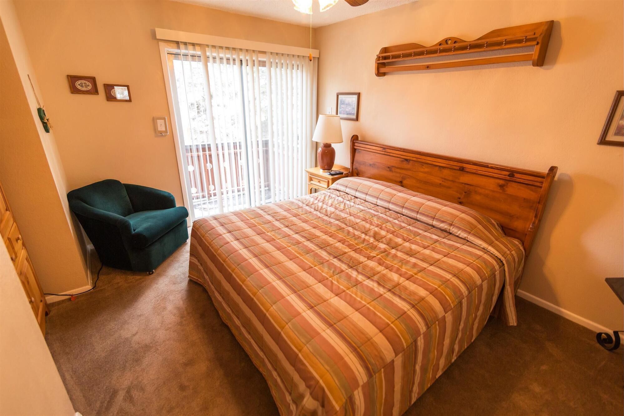 A bedroom with a bed, a chair, a nightstand, a lamp, and a window with blinds.