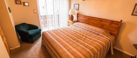 A bedroom with a bed, a chair, a nightstand, a lamp, and a window with blinds.