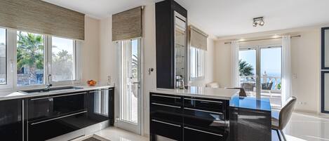 Una cocina moderna con armarios negros, una encimera azul y un amplio ventanal con vistas a un balcón.